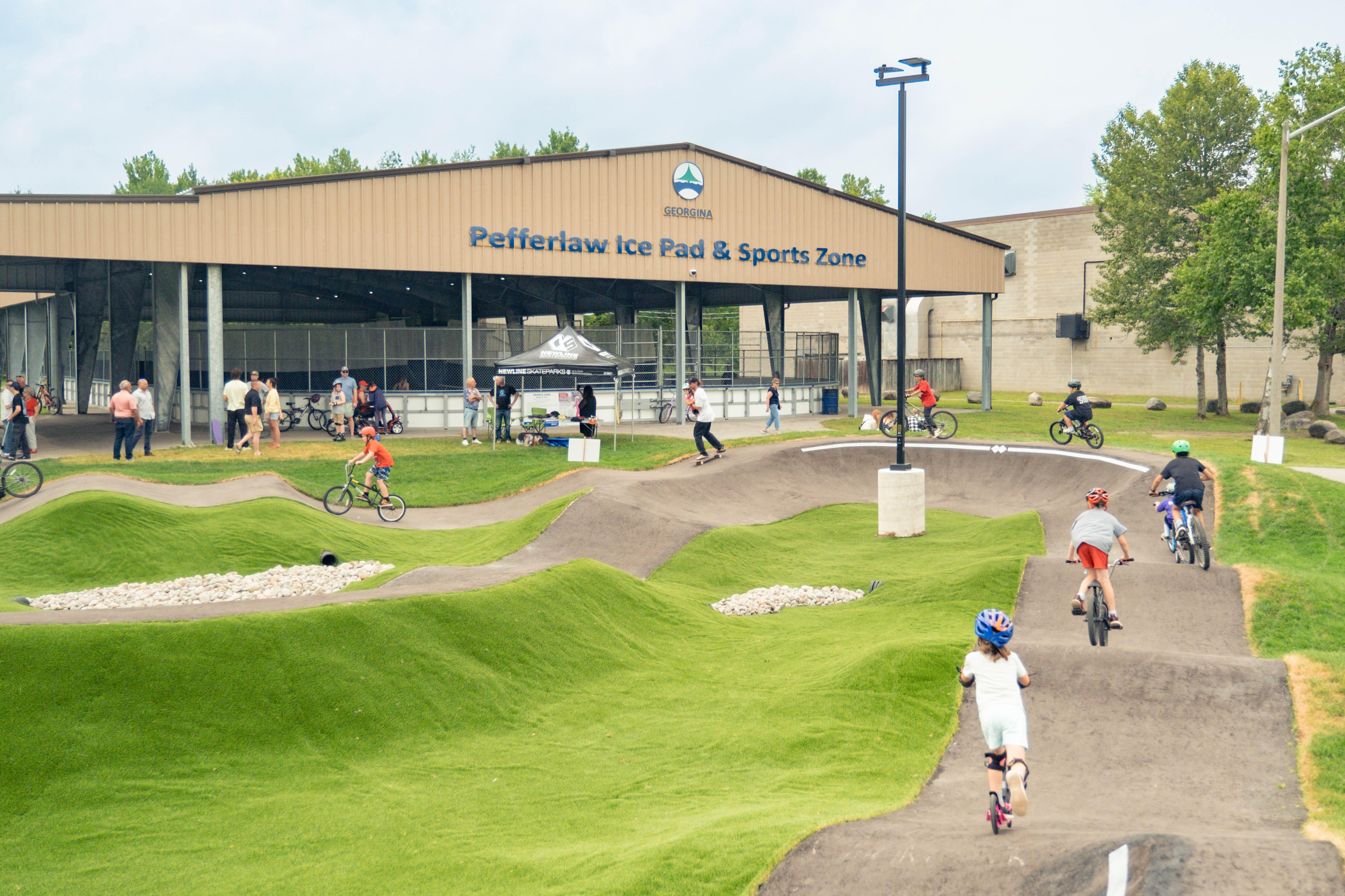 Children on scooters and bikes on cement pathway with Building in the background